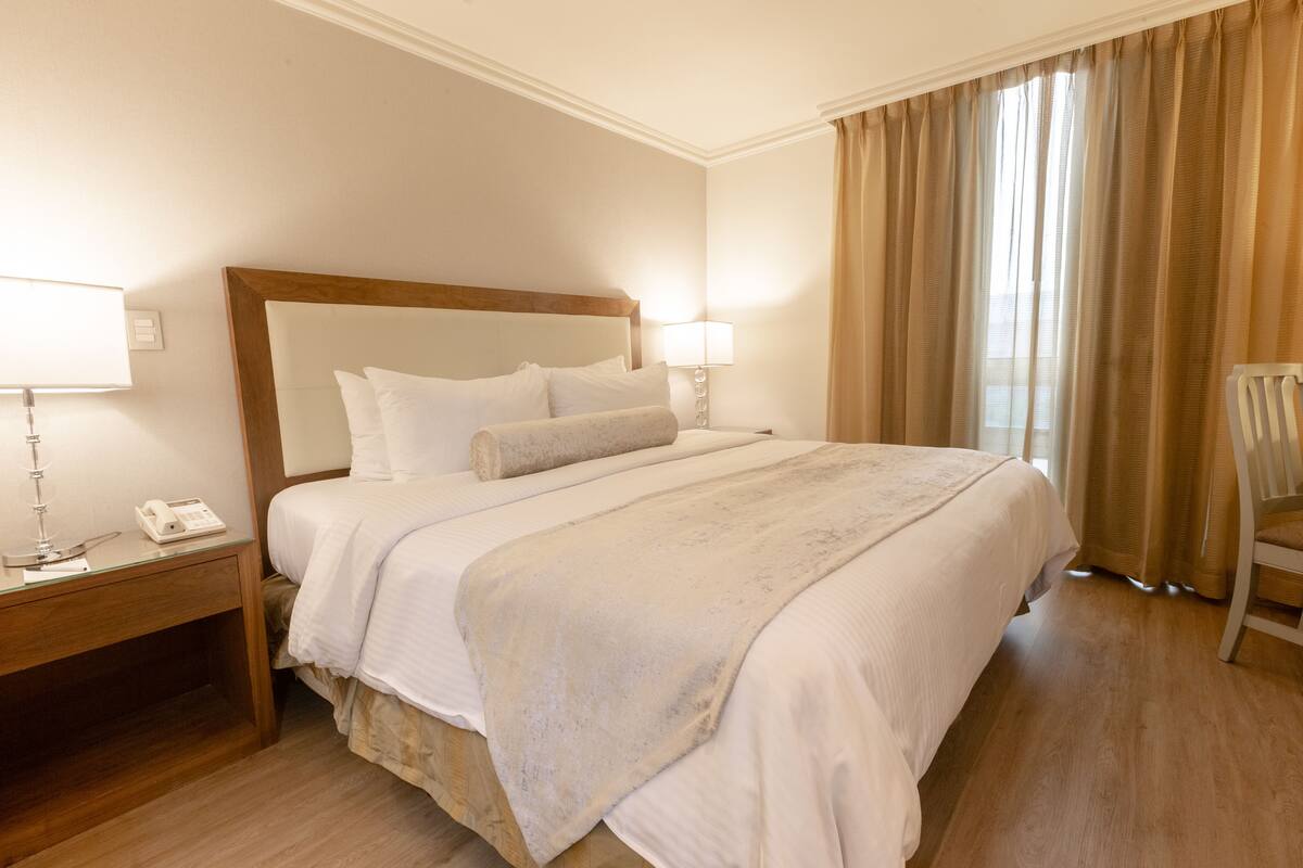 A hotel room with a large bed, wooden headboard, bedside tables with lamps, and a chair.