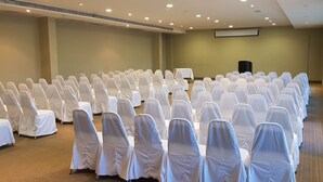 A conference room with rows of white-covered chairs and tables, a projector screen, and a large speaker. - Antaris Cintermex (Monterrey)