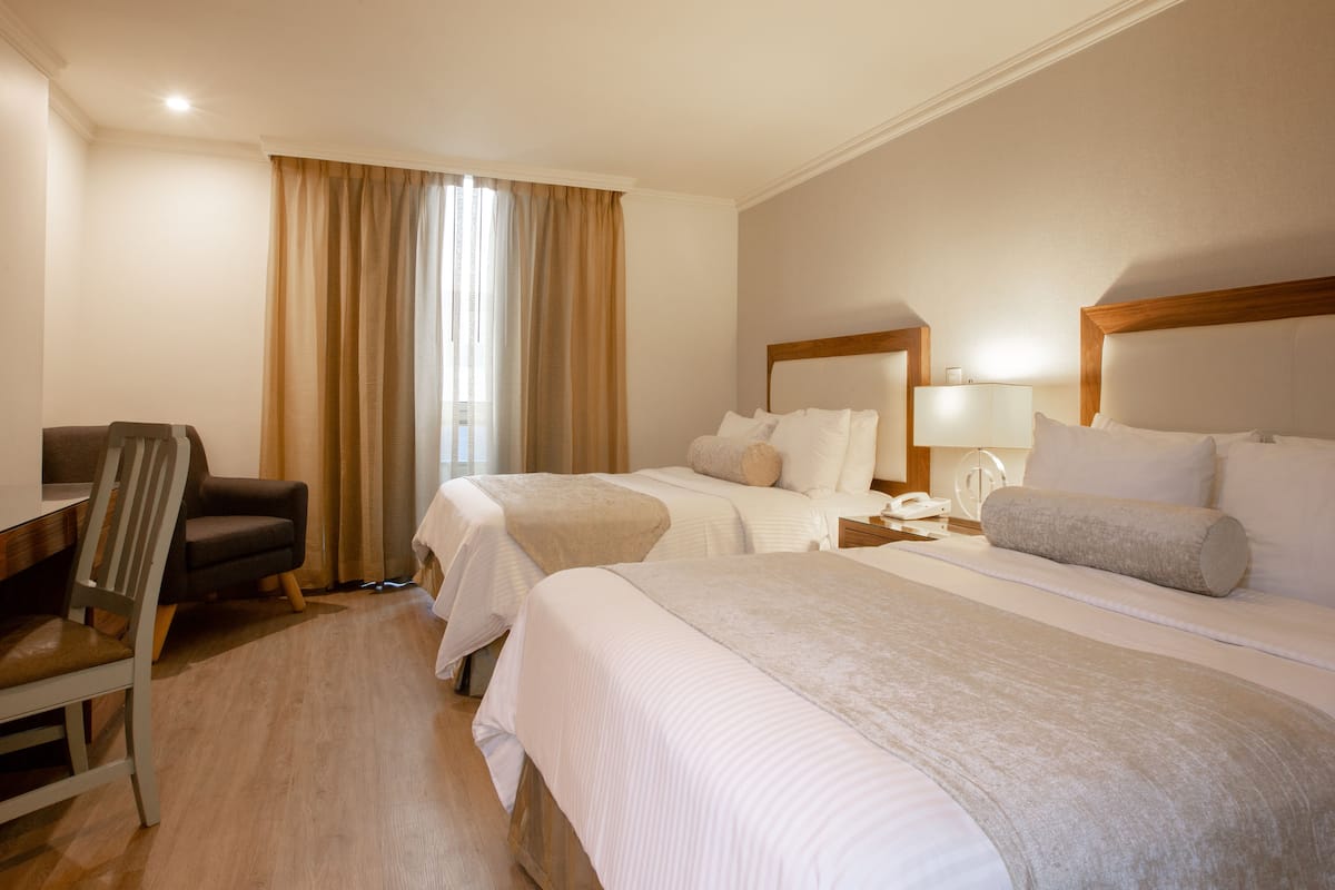 A hotel room with two beds, a desk, a chair, and a window with curtains.
