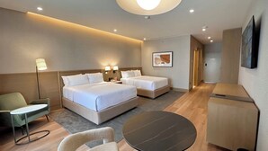 Habitación de hotel con cama, dos mesitas de noche, un escritorio, una silla, una mesa redonda y una televisión.