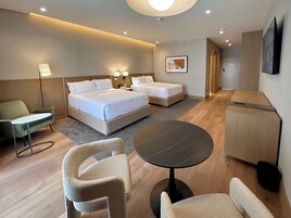 A hotel room with a bed, two bedside tables, a desk, a chair, a round table, and a TV.