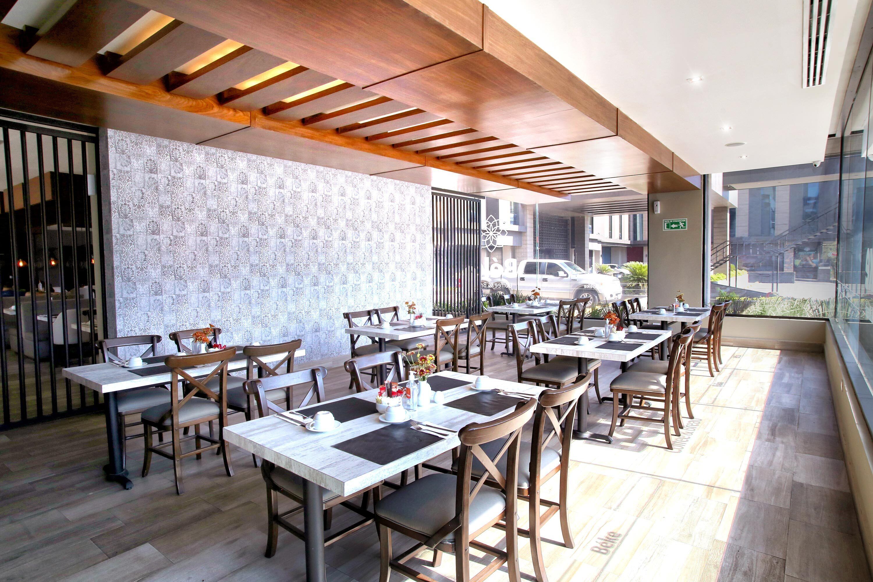 A restaurant with multiple tables and chairs, a patterned wall, and a view of the street outside.