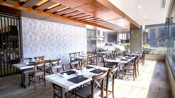 Un restaurante con varias mesas y sillas, un muro decorado y vistas a la calle.