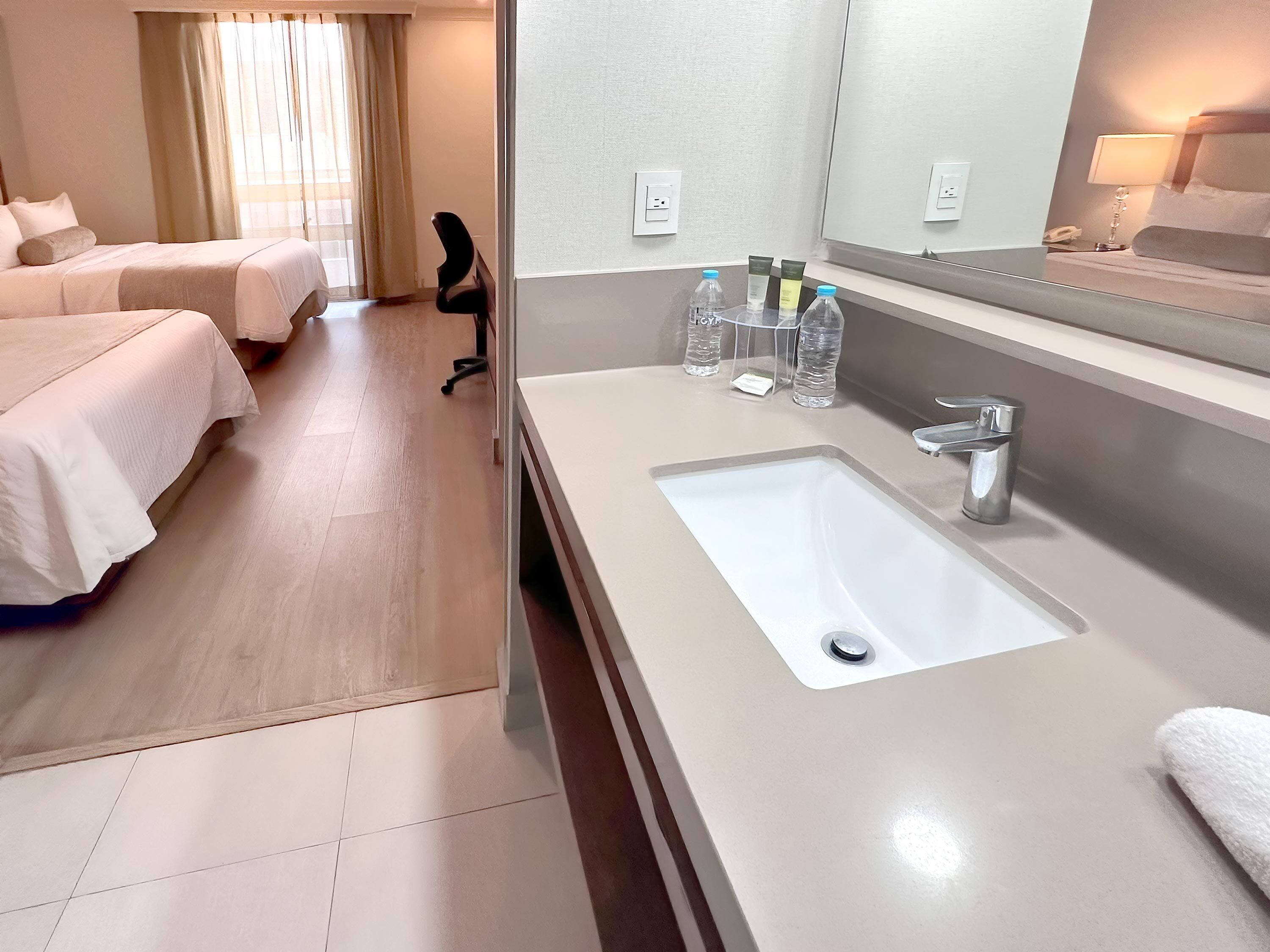 A hotel room with a bed, a desk, a bathroom with a sink, and toiletries.