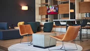 A modern lounge area with a central coffee table, seating with metal legs, and a television mounted on the wall.