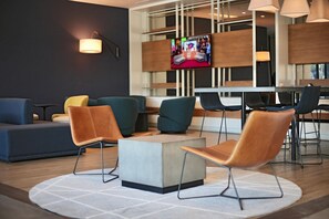 A modern lounge area with a central coffee table, seating with metal legs, and a television mounted on the wall. - Antaris Cintermex (Monterrey)