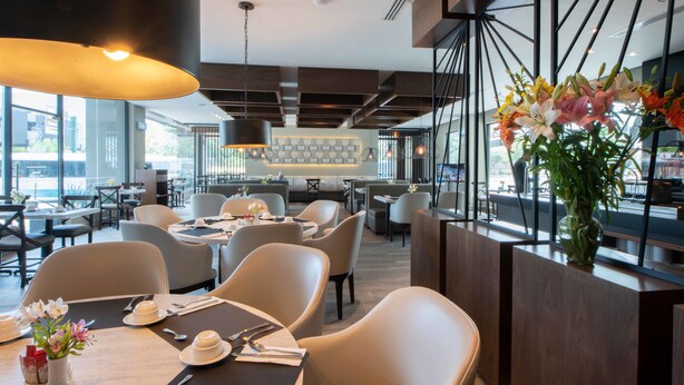 A modern restaurant with high ceilings, large windows, and a variety of seating arrangements. - Antaris Cintermex (Monterrey)