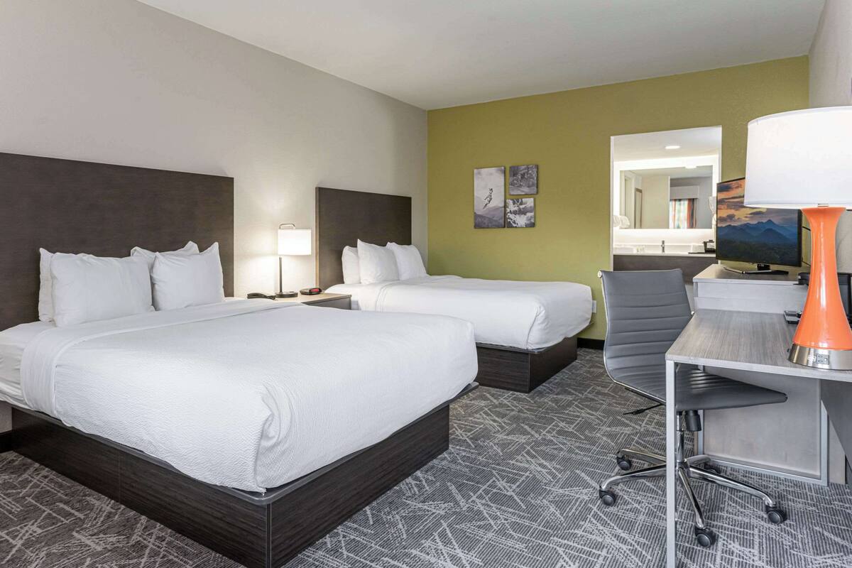 A hotel room with two beds, a desk with a lamp, a chair, and a television.