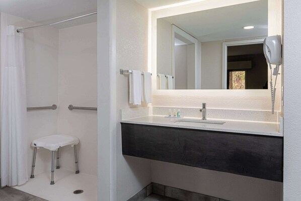 A bathroom with a shower, a white toilet, a vanity with a mirror, and a hairdryer mounted on the wall.
