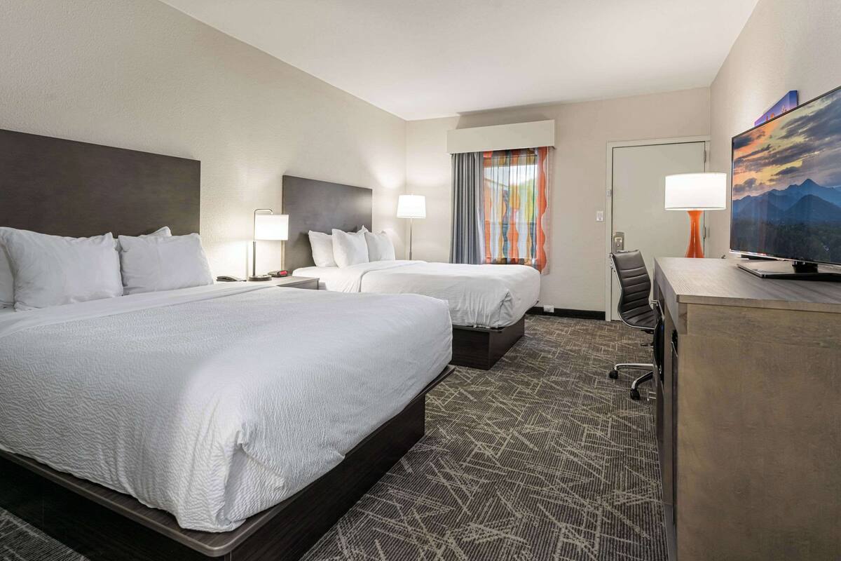 A hotel room with two beds, a desk, a TV, and a window with curtains.