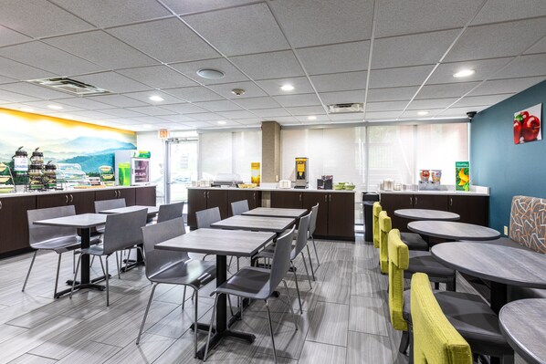 A modern restaurant with multiple dining areas, including booths and tables. There are kitchen counters visible in the background, and the space is well-lit with ceiling lights.