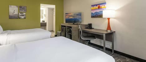 A hotel room with two beds, a desk, a television, and a lamp.