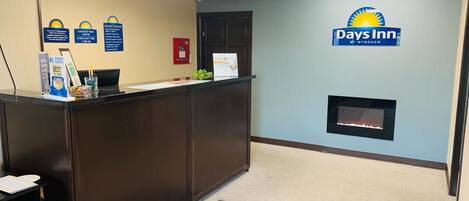 A reception area with a dark wooden desk, a fire screen, and a Days Inn logo on the wall.