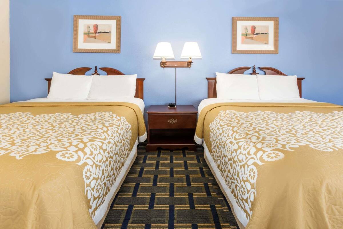 A hotel room with two single beds, a nightstand with a lamp, and two framed pictures on the wall.