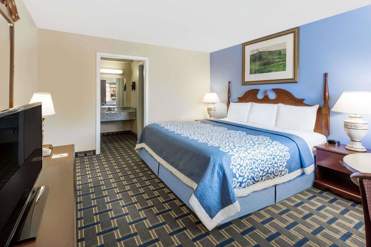A hotel room with a bed, a television, a desk, and a bathroom visible through an open door.