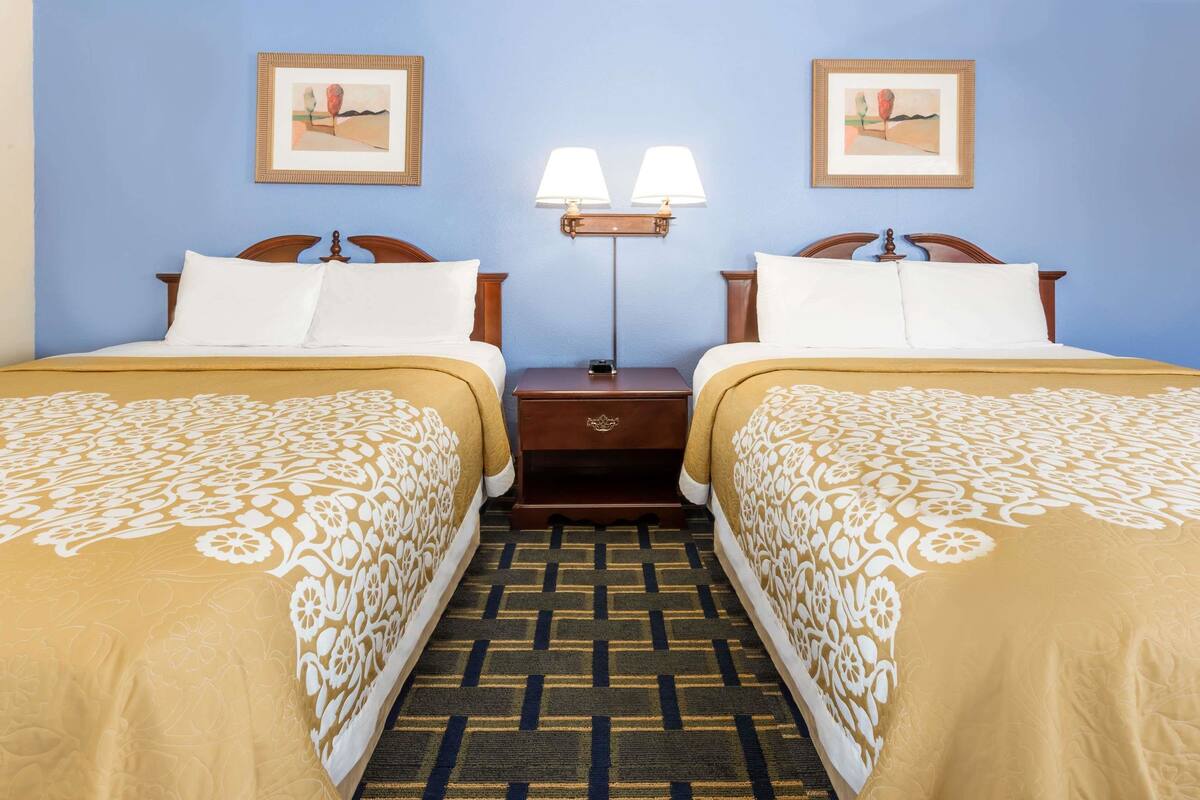 A hotel room with two single beds, a nightstand with a lamp, and two framed pictures on the wall.