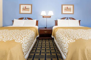 Una habitación de hotel con dos camas individuales, una mesita de noche con lámpara y dos cuadros enmarcados en la pared.