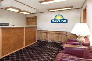 Una zona de recepción con un escritorio de madera, una computadora, una lámpara y el logotipo de Days Inn en la pared.