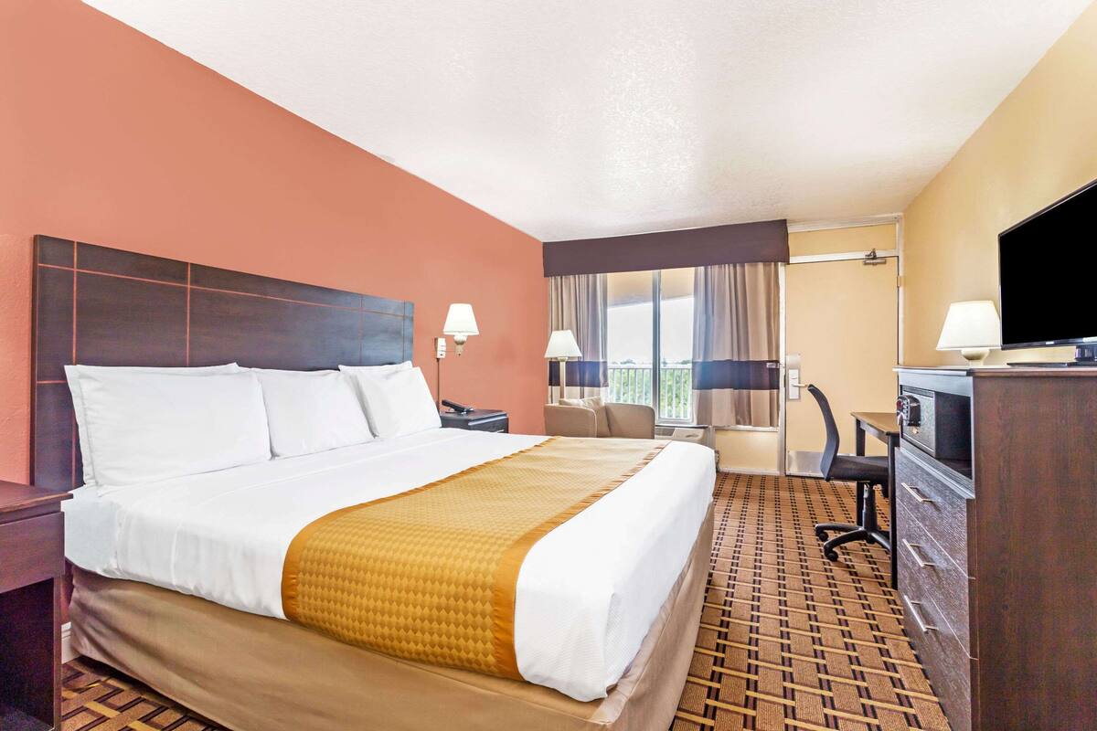 A hotel room with a large bed, a desk, a chair, and a television.