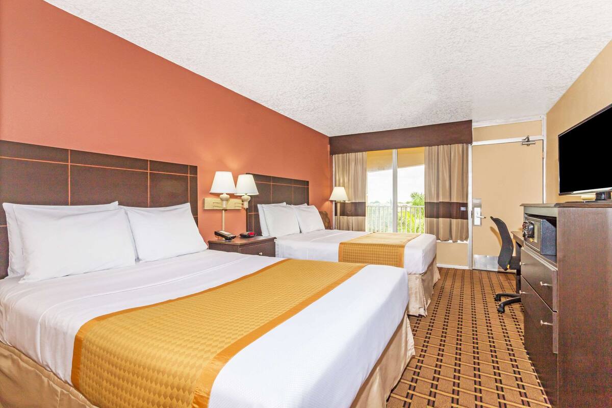 A hotel room with two beds, a desk with a TV, and a window with curtains.