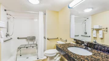 A bathroom with a white toilet, a sink with a granite countertop, a shower with a grab bar, and a mirror with a towel rack.