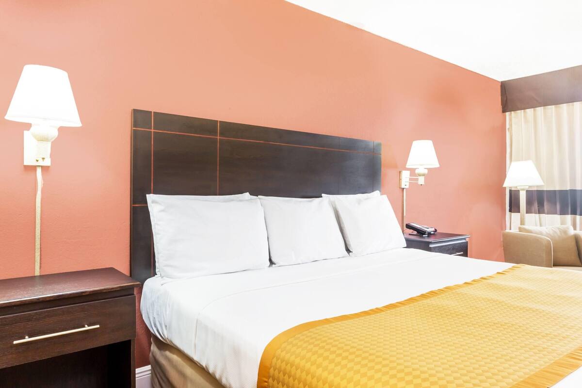A hotel room with a bed, bedside tables, lamps, and a chair.