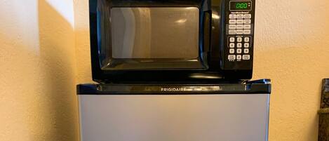 A compact, stainless steel refrigerator with a digital microwave on top.