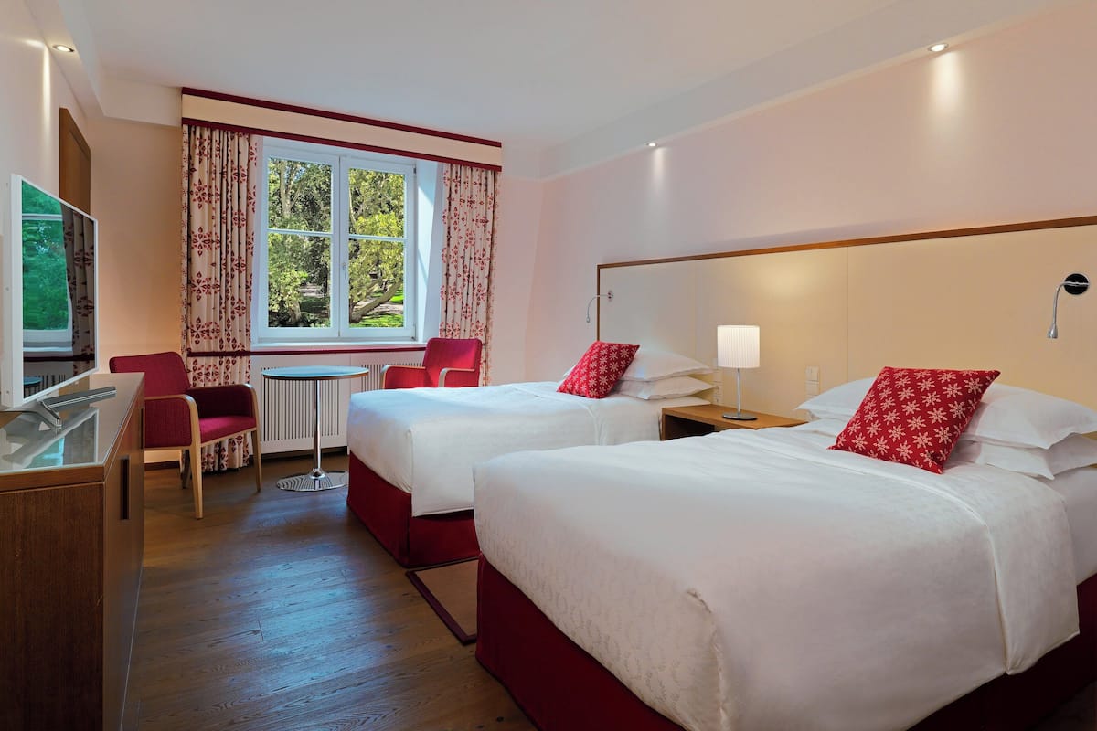 Habitación de hotel con dos camas, un escritorio, una silla y una ventana con cortinas.