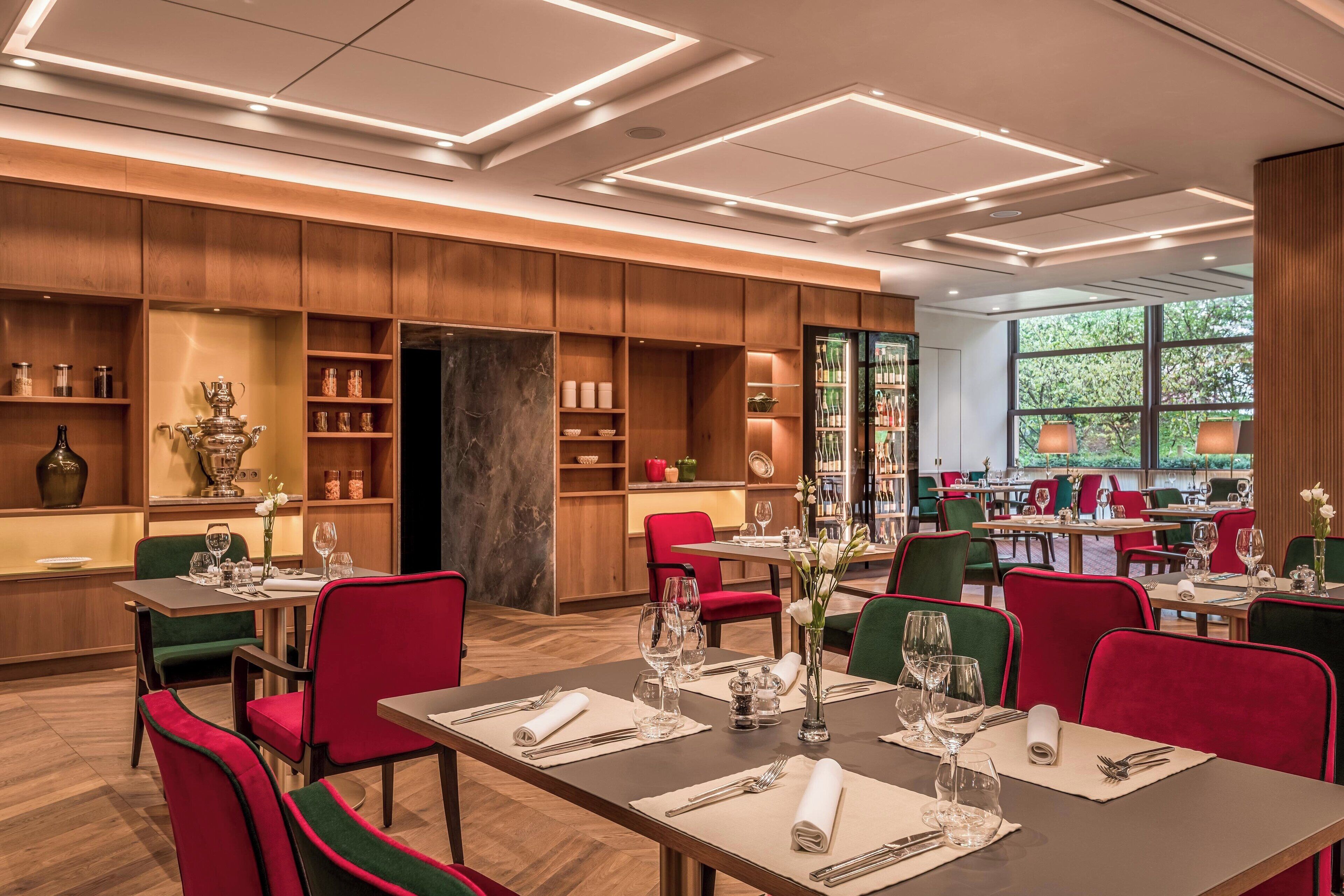 Ein Restaurant mit Holzwandverkleidung, rot- und grün gepolsterten Stühlen und Tischen, die mit weißen Servietten und Weingläsern gedeckt sind.