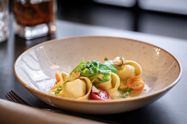 Un tazón de pasta con verduras y tomates cherry sobre una mesa.
