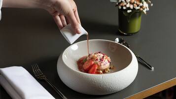 A hand pouring a liquid into a white bowl with a dessert on top.
