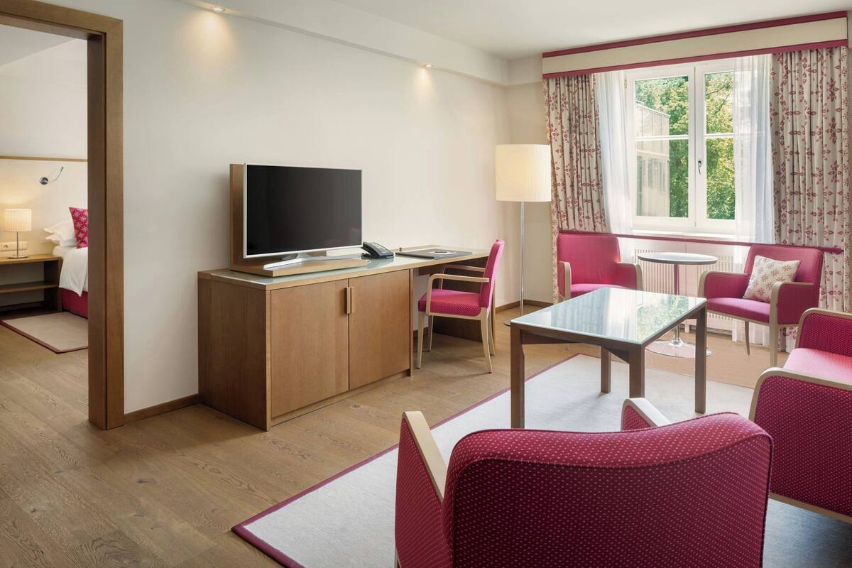 Habitación de hotel con escritorio de madera, televisor, sofá y ventana con cortinas.