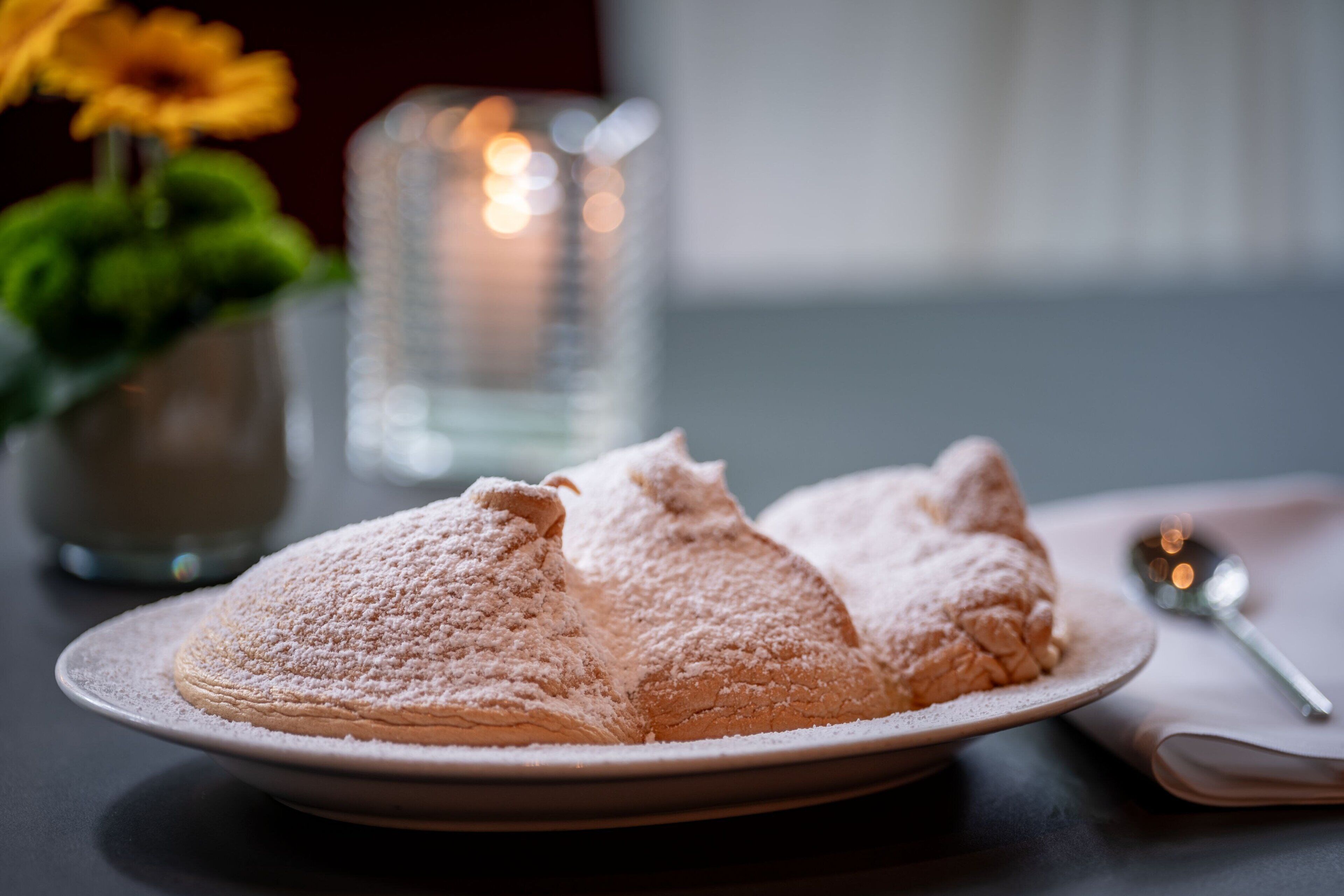 A plate of pastries dusted with powdered sugar, a spoon, and a candle in the background.