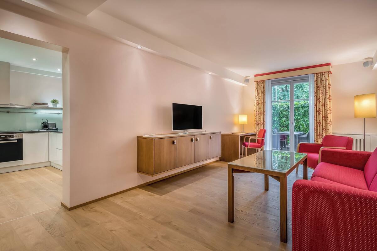 Una sala de estar moderna con una mesa de centro de vidrio, sofás rojos y un televisor sobre un mueble de madera.