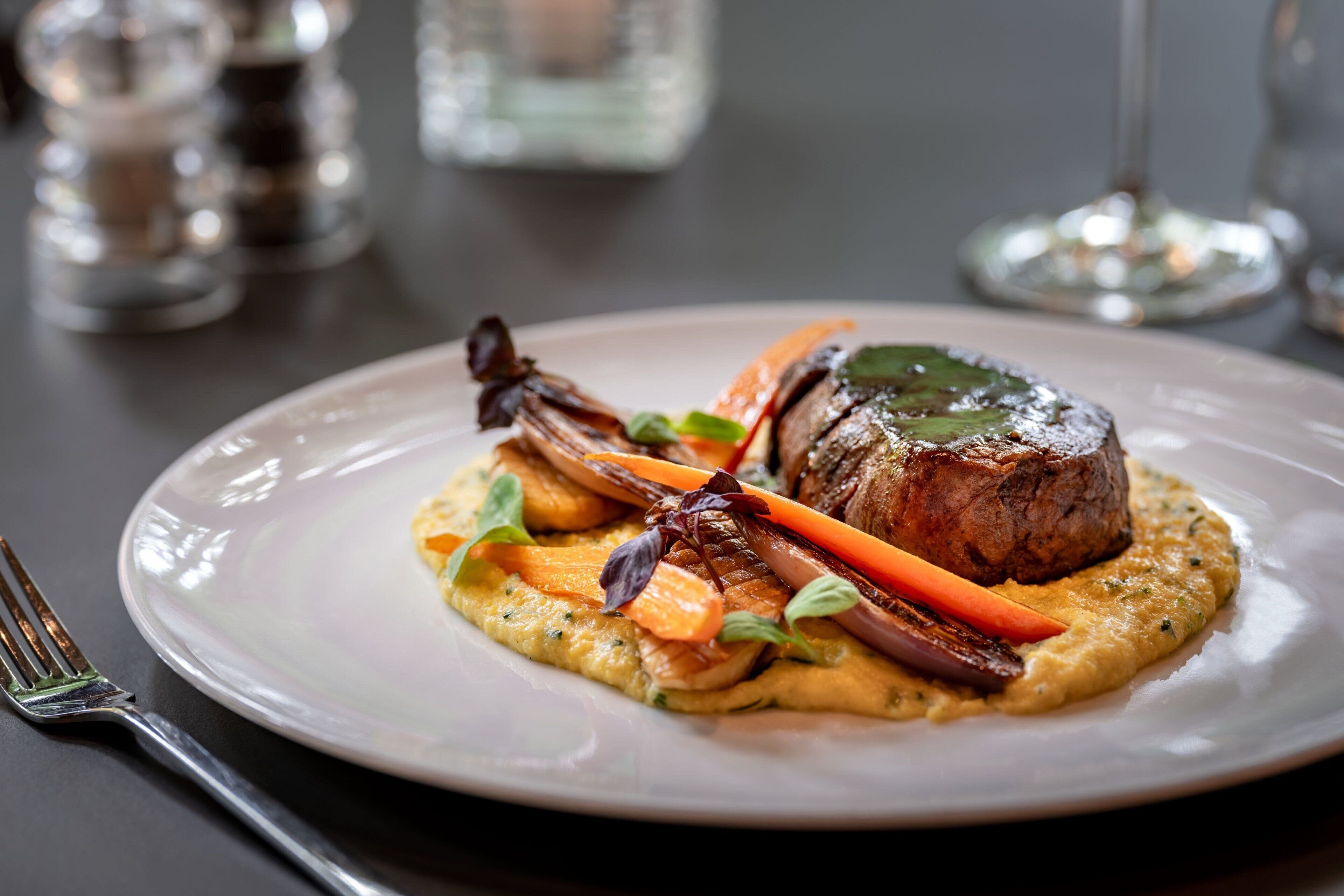 A plate of food with a steak, vegetables, and a creamy sauce.