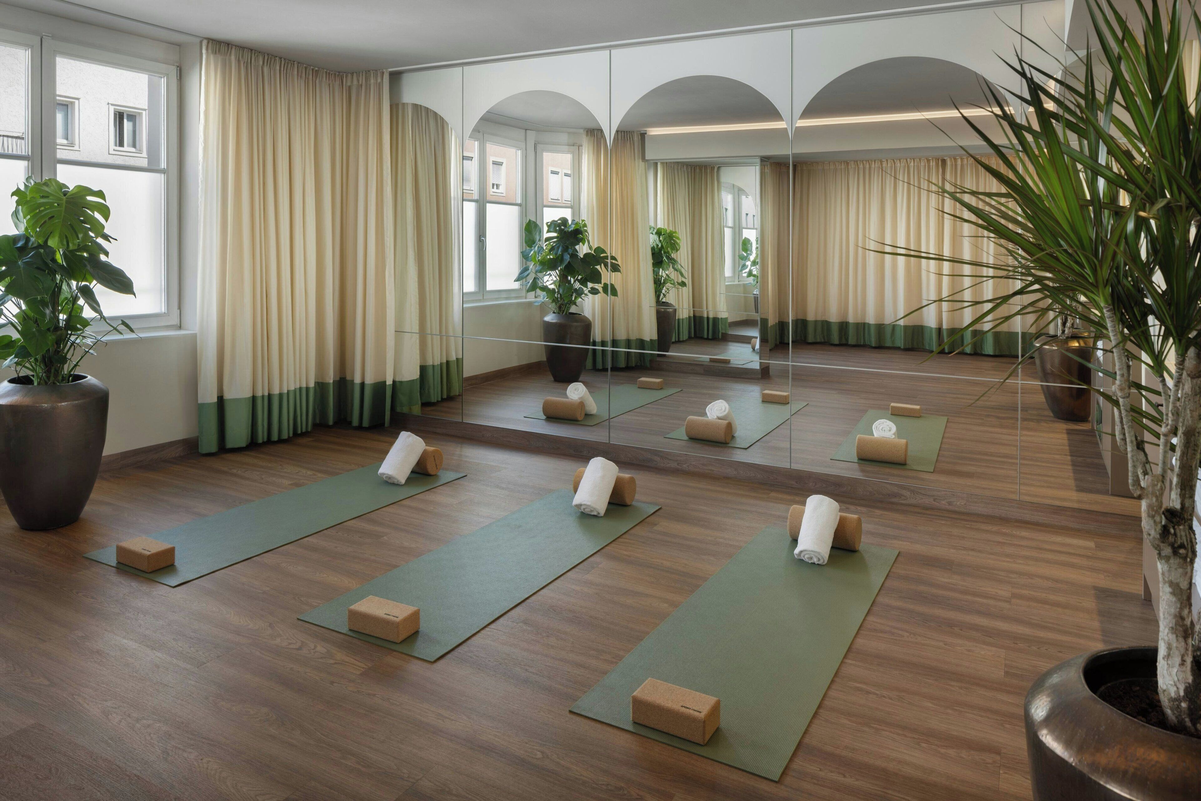 Une pièce dotée d’un plancher en bois, de tapis de yoga et d’un grand miroir qui reflète l’espace.