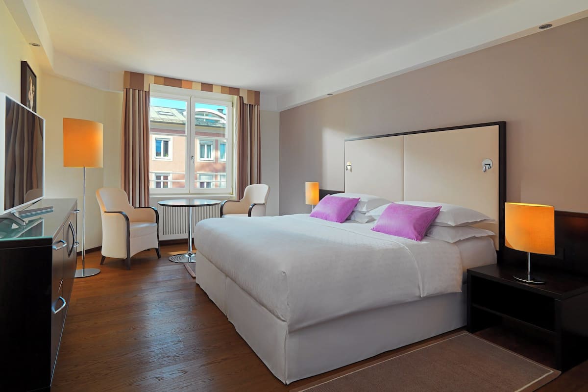 Habitación de hotel con una cama grande, un escritorio con ordenador, una silla y una ventana con cortinas.