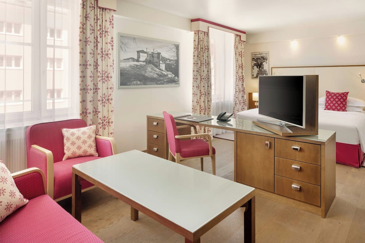 Habitación de hotel con cama, escritorio con silla, televisor y ventana con cortinas.