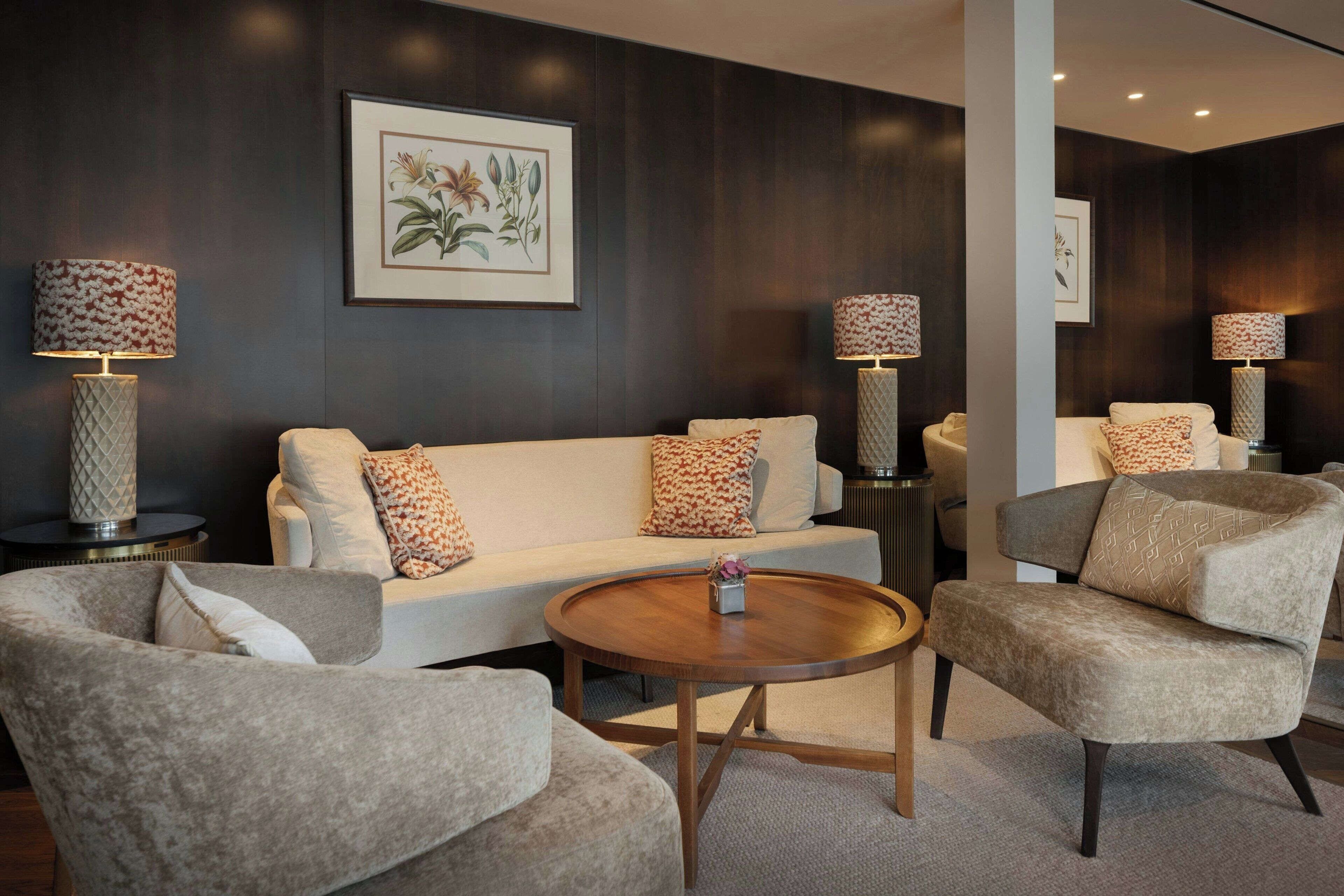 A modern living room with a white sofa, two armchairs, a round coffee table, and two floor lamps with patterned shades.