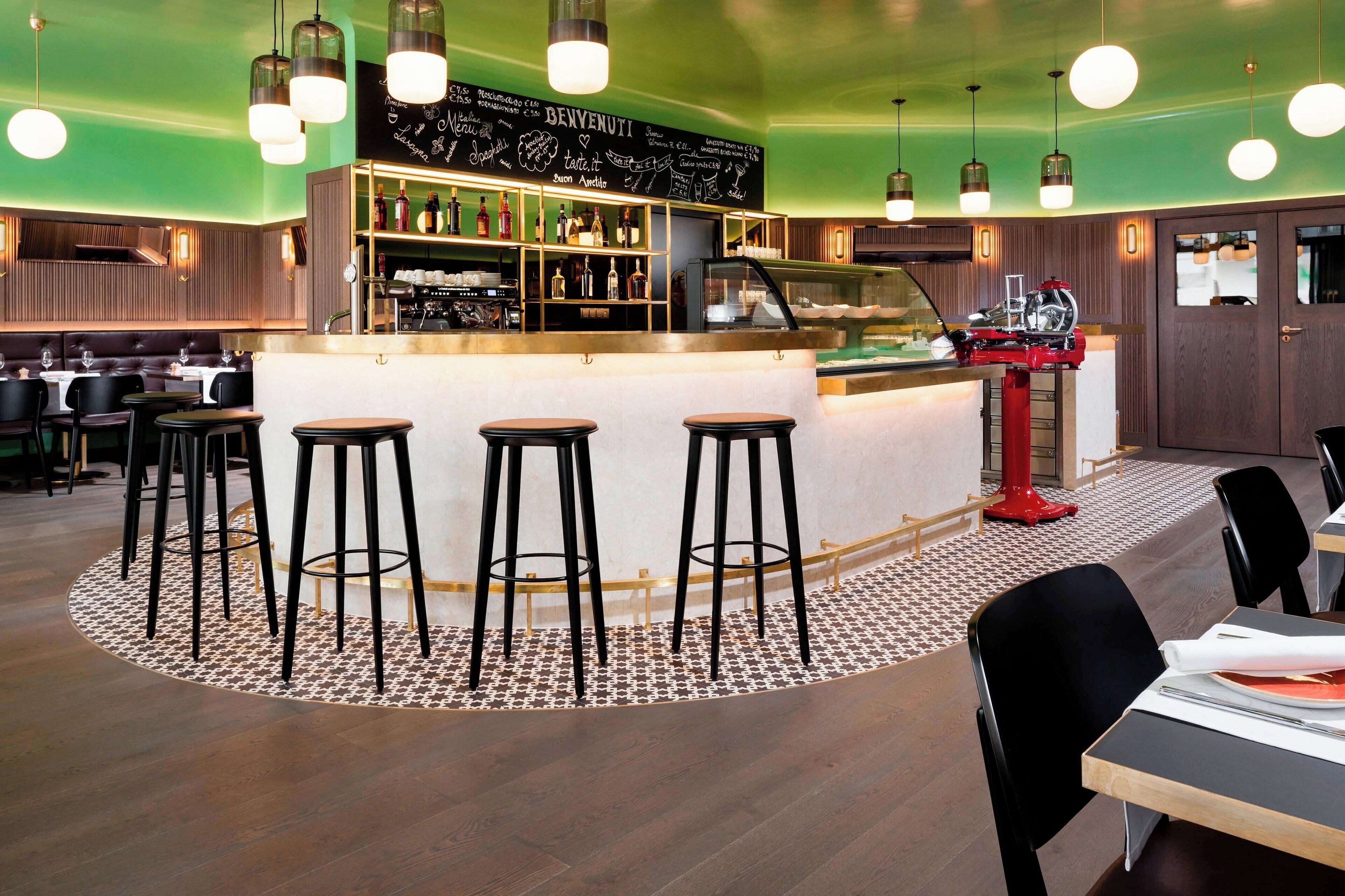 A bar area with stools, a counter with a cash register, and shelves with bottles.