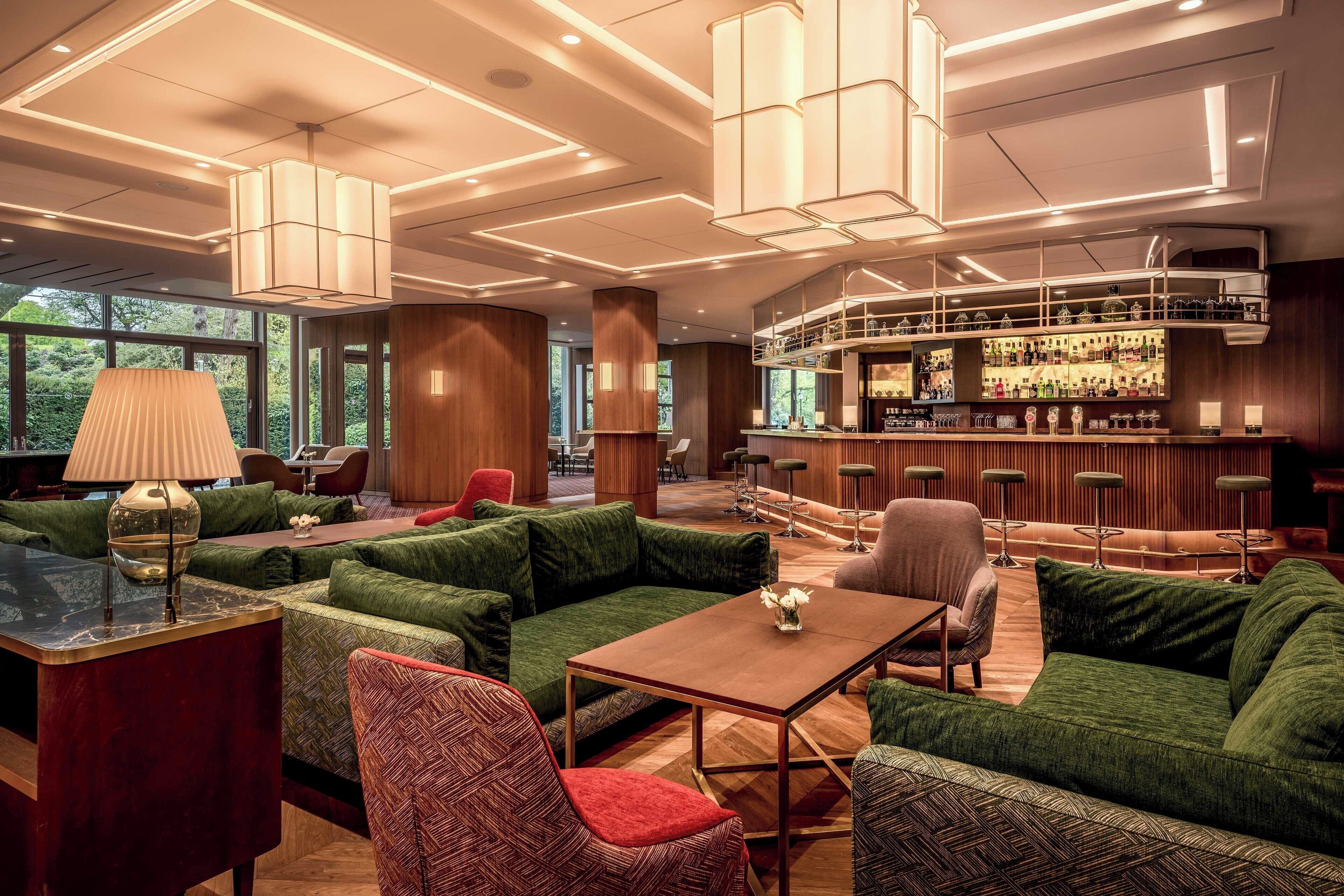 Un espacio lounge moderno con sofás tapizados en verde, una barra de madera e iluminación ambiental.
