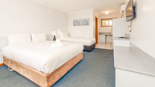 A hotel room with a large bed, a smaller bed, a desk, a flat-screen TV, and a painting on the wall. - Seasonal South Motel & Function Centre (Ulverstone)