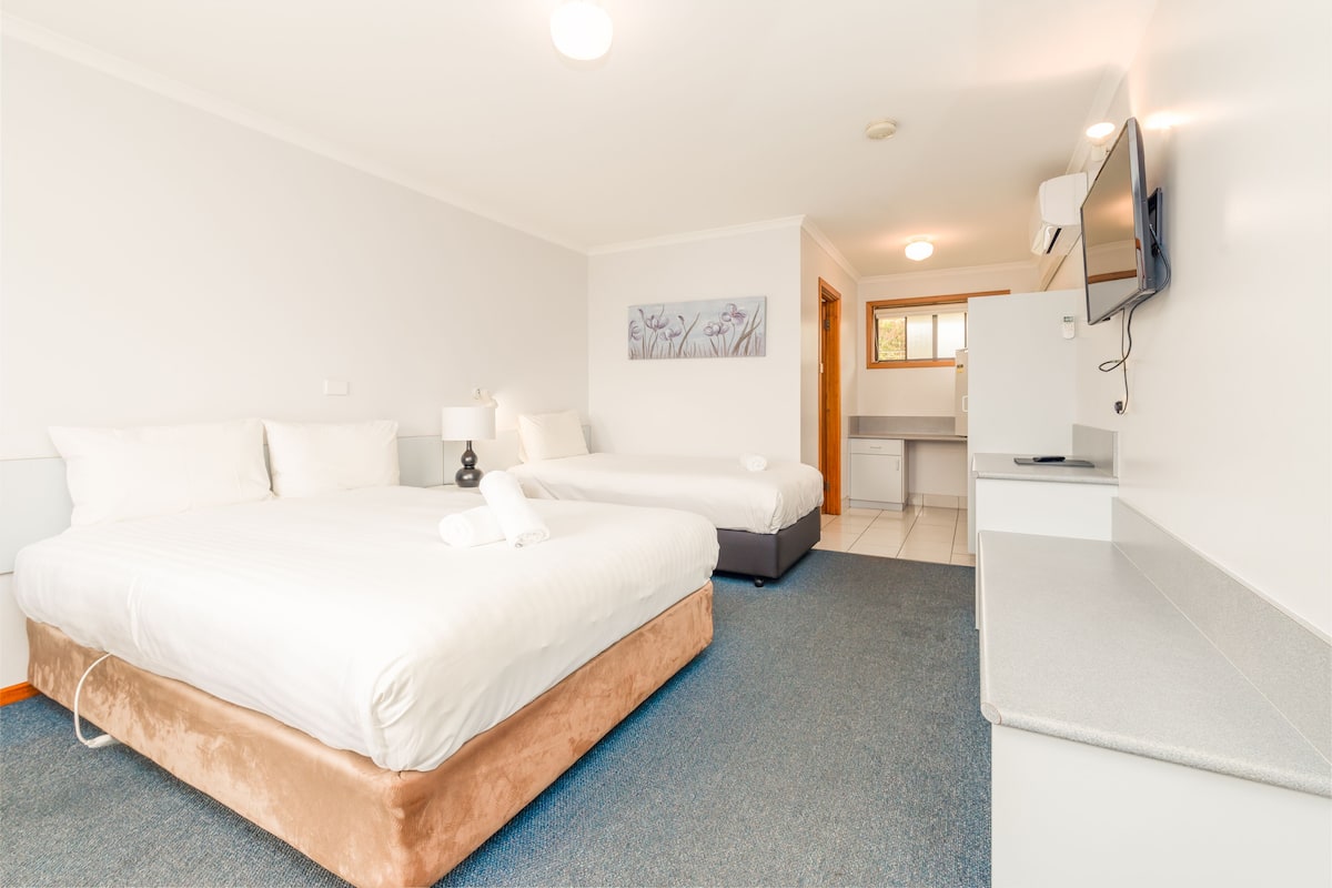 A hotel room with a large bed, a smaller bed, a desk, a flat-screen TV, and a painting on the wall.