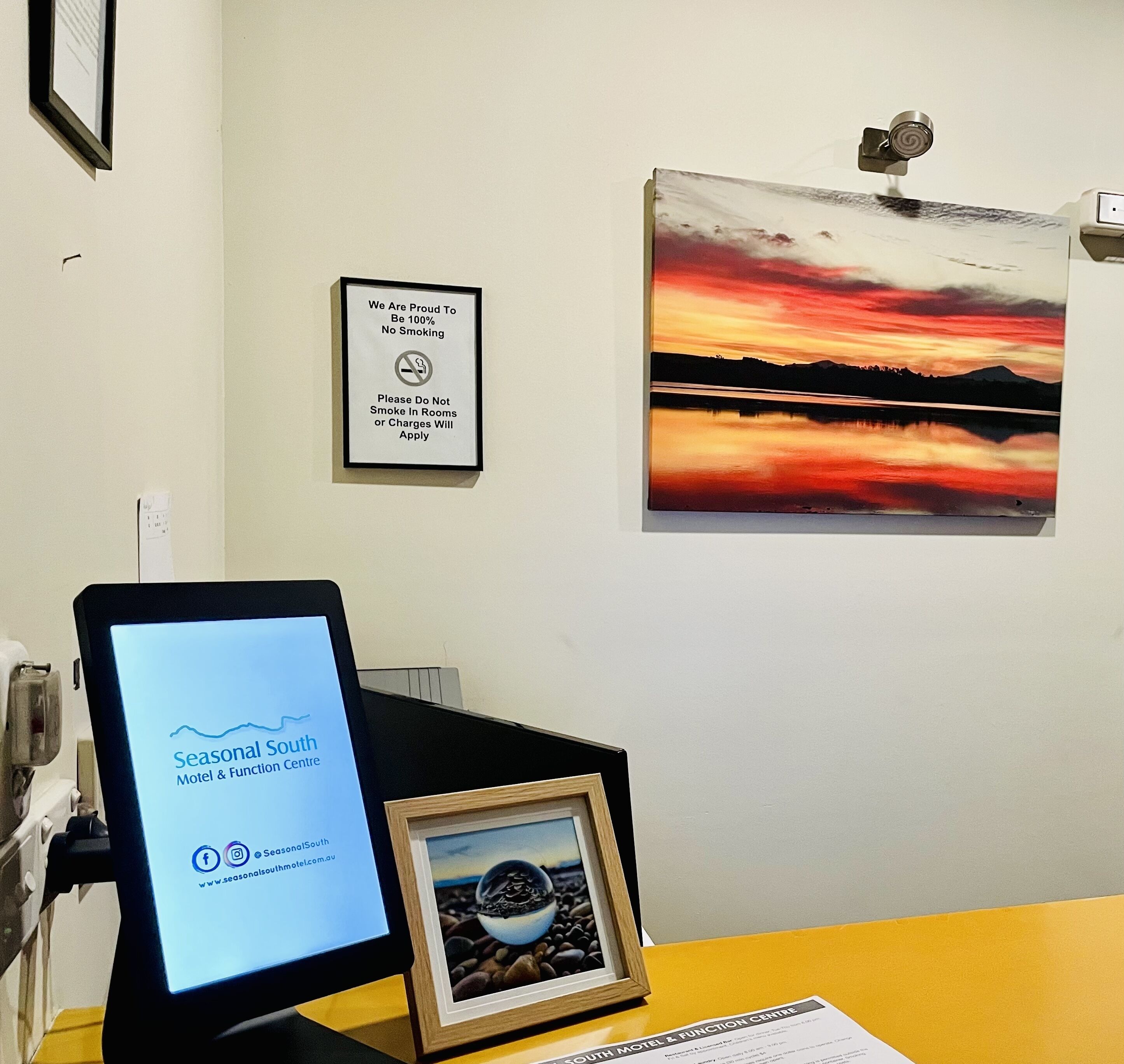 A desk with a computer monitor displaying the Seasonal South Motel & Function Centre website, a framed picture of a beach scene, and a no-smoking sign on the wall.