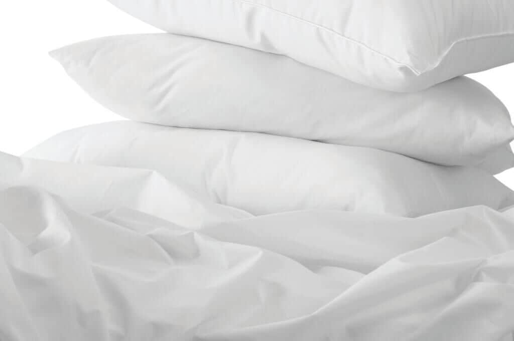 Ein Stapel weißer Kissen auf einem Bett mit weißen Laken.