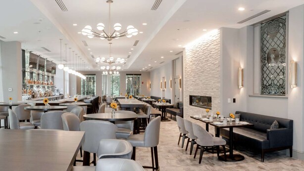 Un restaurant moderne avec des tables rondes, des chaises grises et un bar doté d’étagères.