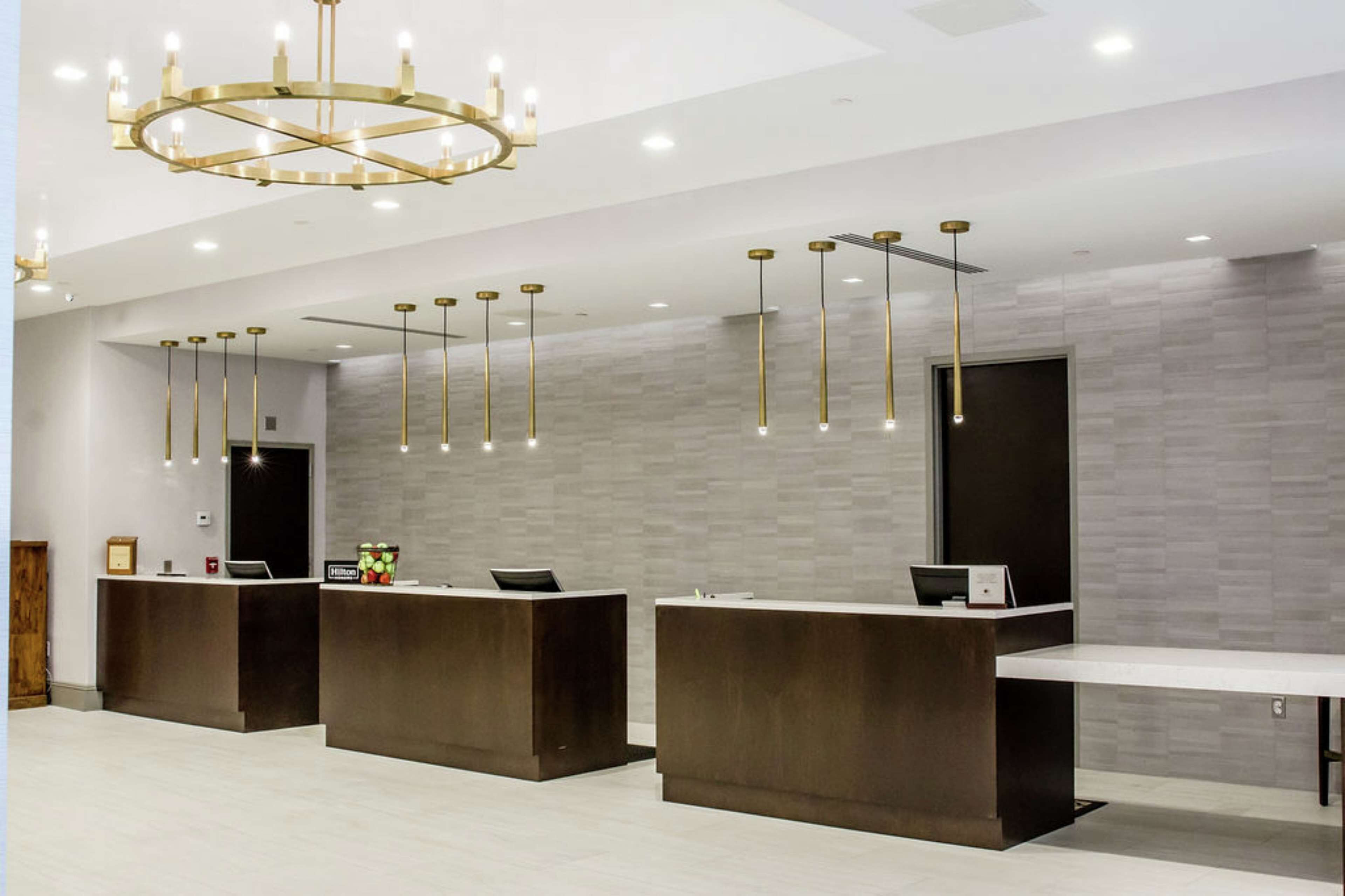 A modern reception area with three dark reception desks, a large chandelier, and pendant lighting.