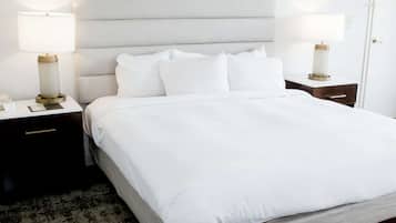 Una cama bien hecha con sábanas blancas, dos mesitas de noche con lámparas y una alfombra oscura en el suelo.