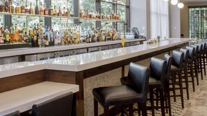 Un espace bar doté d’un long comptoir, de plusieurs luminaires suspendus et d’une variété de bouteilles exposées sur des étagères.