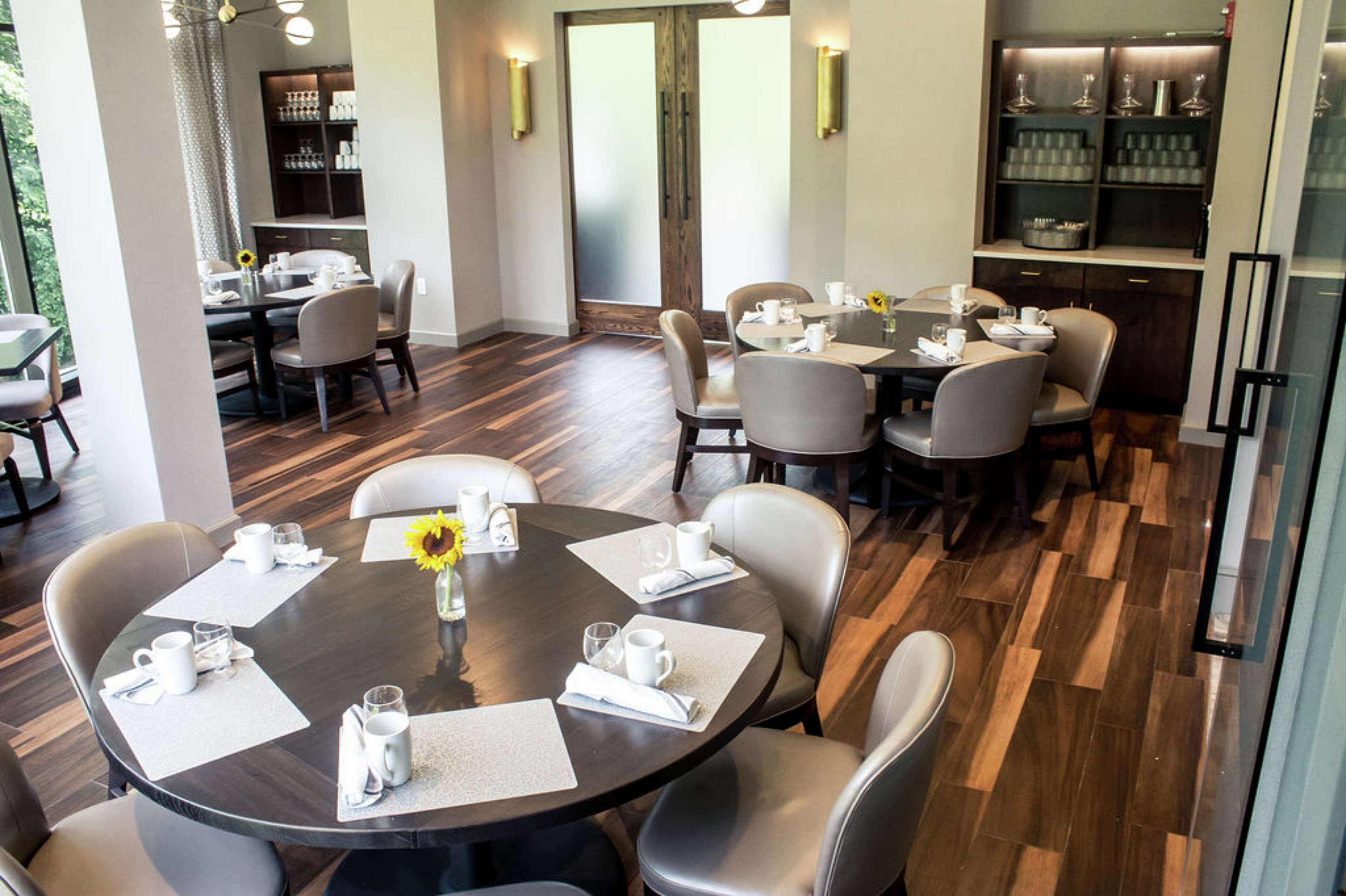 A dining area with round tables, chairs, and a central vase.
